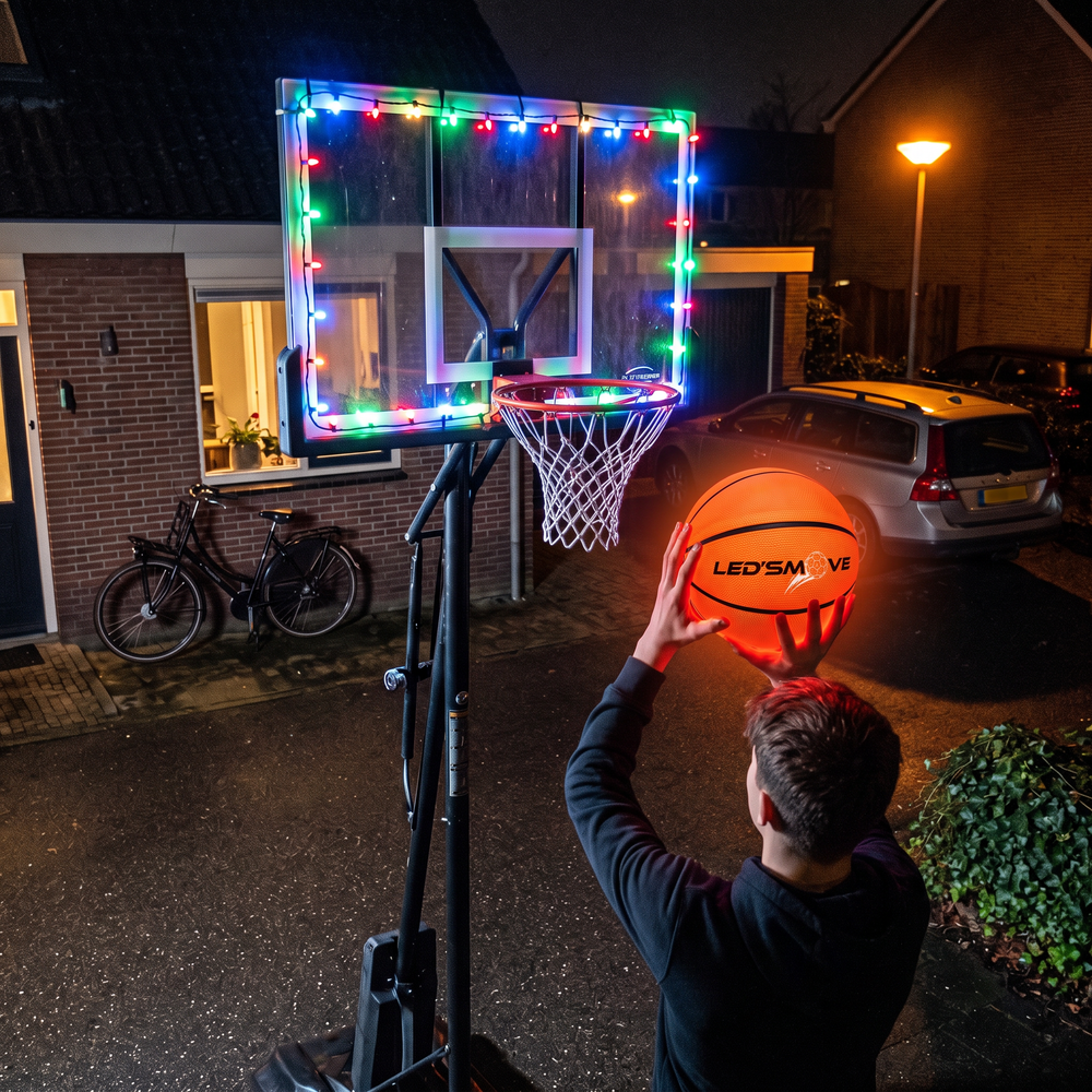 Jongen gooit de lichtgevende basketbal naar een verlichte basketbalring
