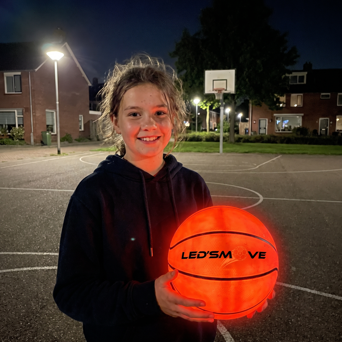 Mädchen mit einem leuchtenden LED-Move-Basketball auf einem kleinen Platz in der Nachbarschaft
