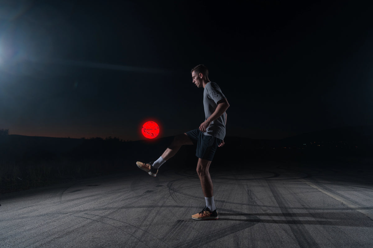 Jongen houdt een rood gloeiende LED bal hoog op een donker veldje