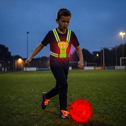 Jongen met lichtgevend hesje en lichtgevende veters speelt met de LED voetbal