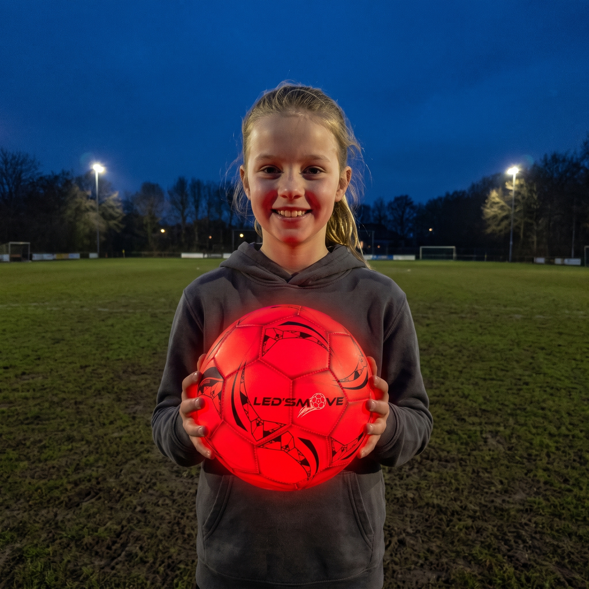 Meisje houdt een lichtgevende LED'S MOVE voetbal vast op het voetbalveld