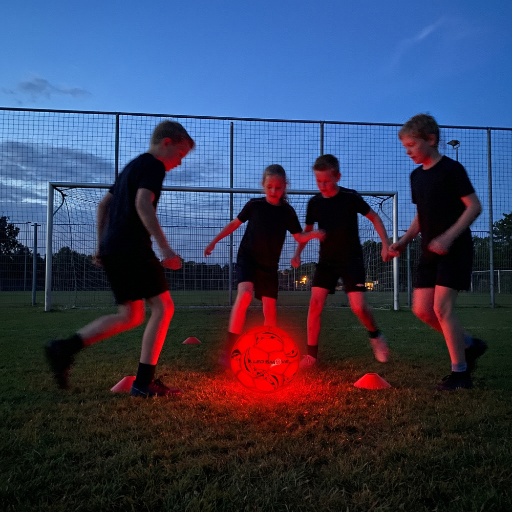 Vier kinderen trainen in de avond met een lichtgevende LED'S MOVE voetbal